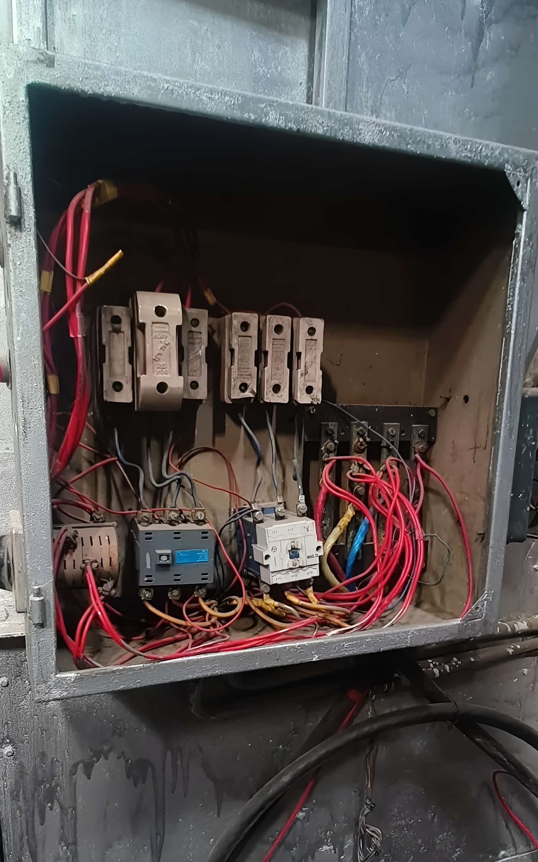 Aged machine electrical panel with worn fuse carriers and tangled red wiring inside an open steel enclosure.